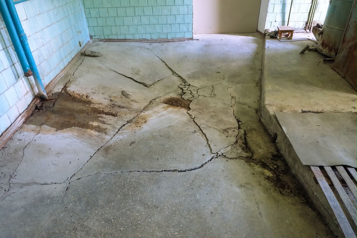 Severely cracked and water-stained concrete basement floor showing hydrostatic pressure damage