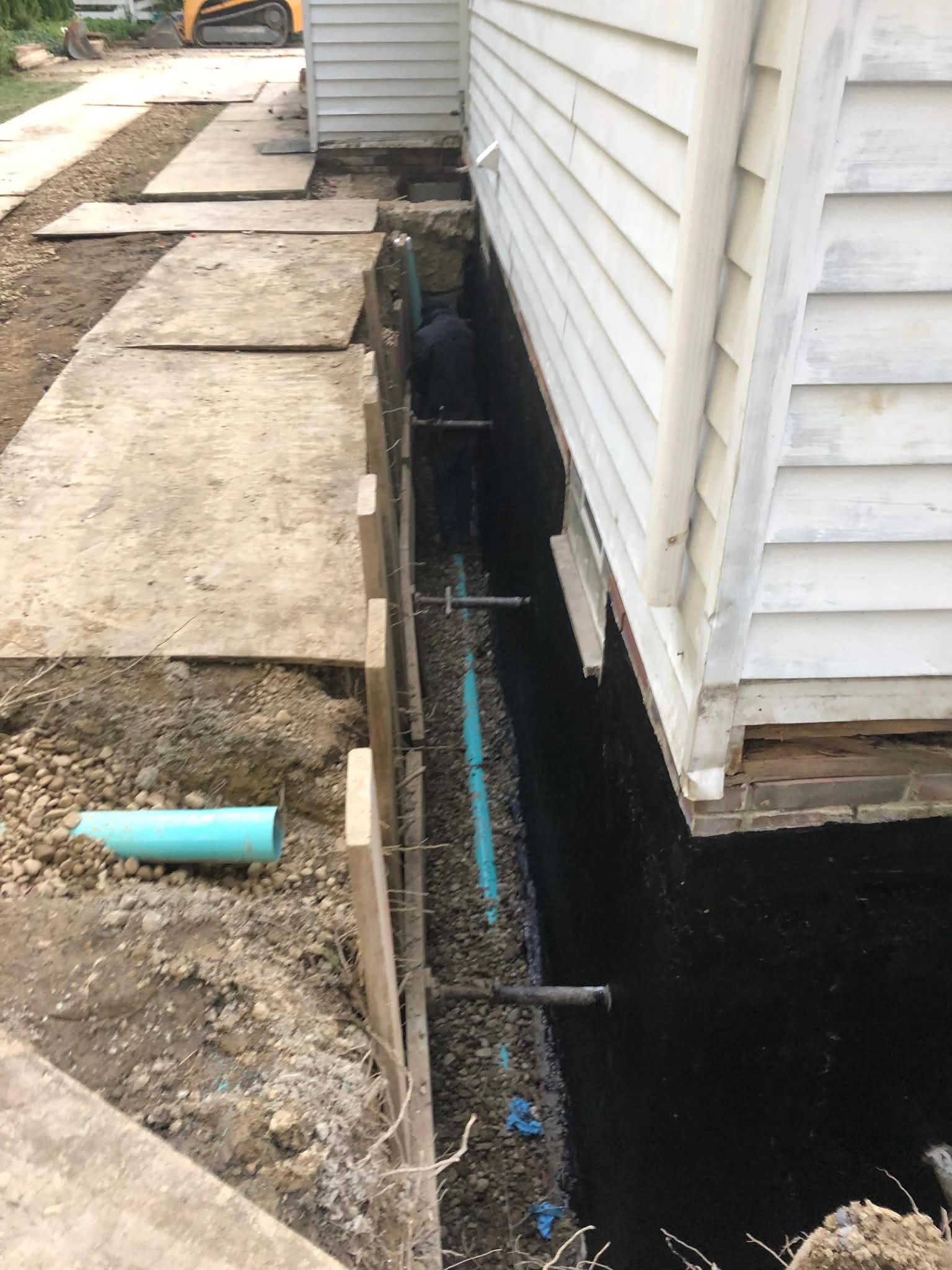 Exterior foundation excavation with waterproofing membrane and underpinning piers installed simultaneously