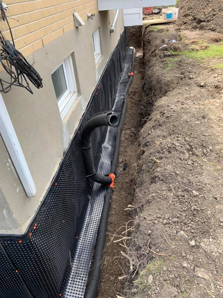 Exterior French drain system with dimple drainage mat and perforated black pipe in graded trench