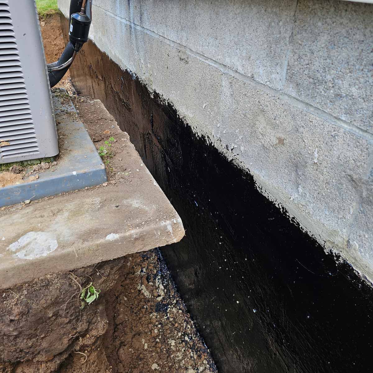 Black exterior waterproofing membrane applied to concrete block foundation wall — seamless barrier against groundwater