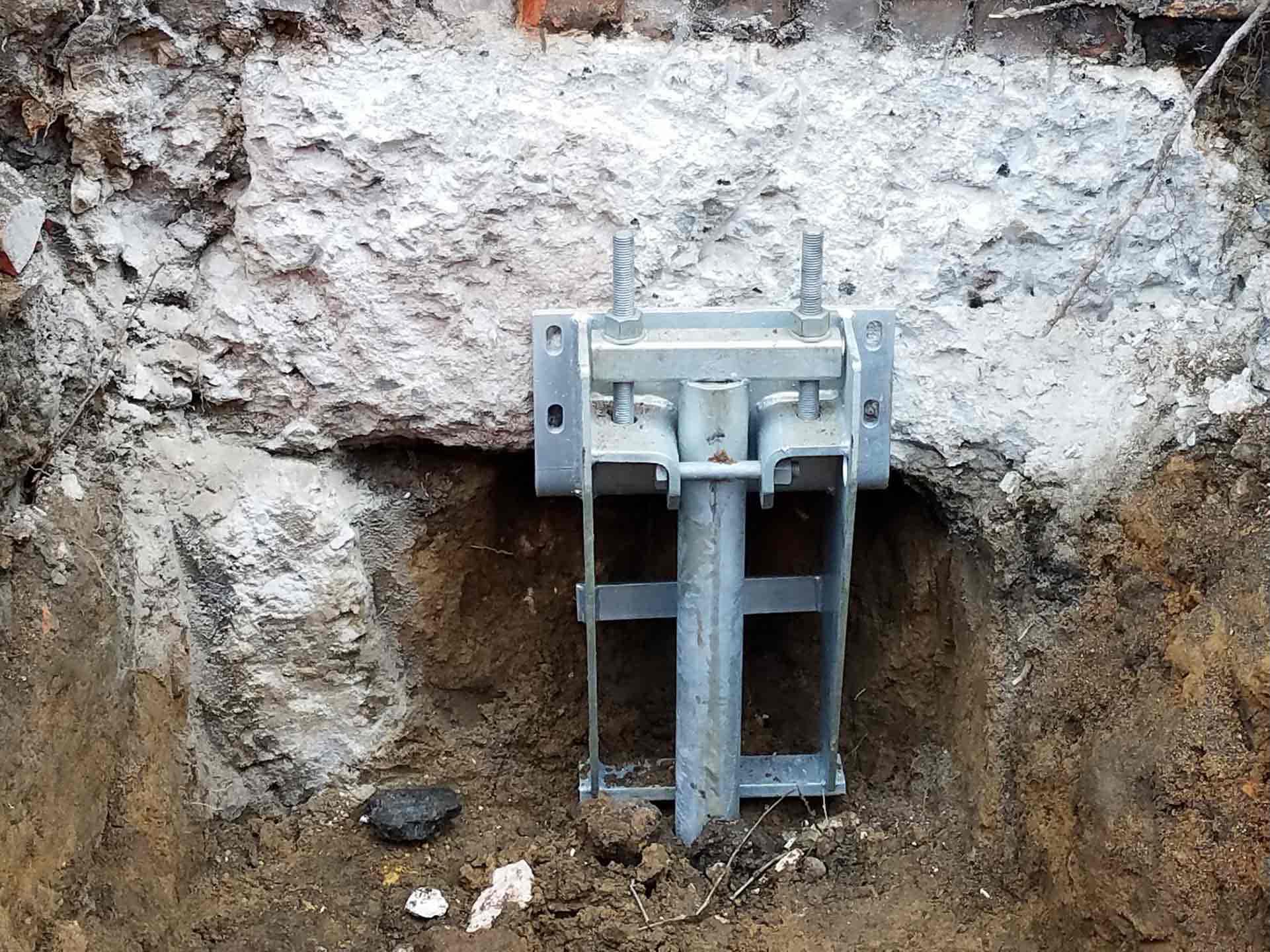 Helical pier bracket installed at poured concrete foundation wall for structural support and stabilization