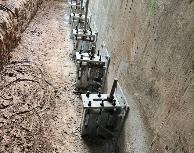 Series of multiple push pier brackets installed along concrete foundation wall for full-wall stabilization