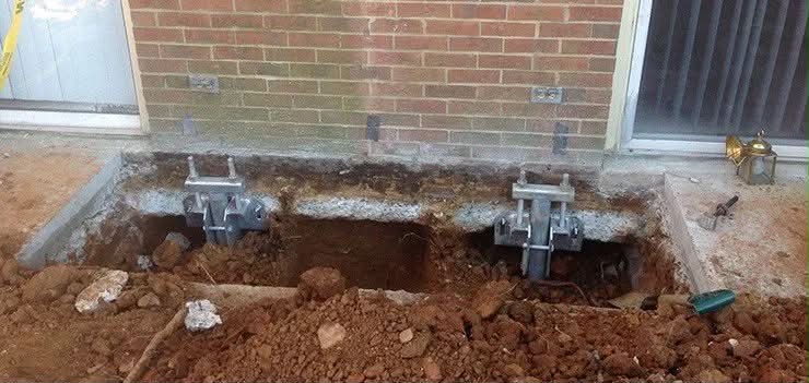 Two push pier brackets installed at brick foundation base for structural stabilization