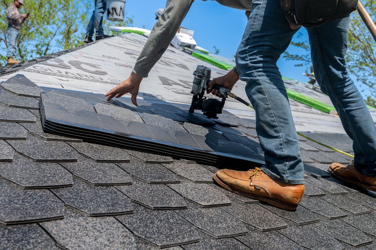 Crew installing architectural asphalt shingles with nail guns on residential roof